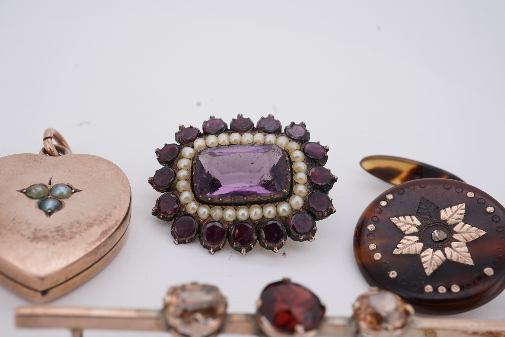 A Victorian yellow metal, amethyst and garnet cluster set brooch, 22mm, an early 20th century yellow metal and seed pearl set heart shaped locket, a yellow metal, garnet and zircon set three stone bar brooch and a tortoi